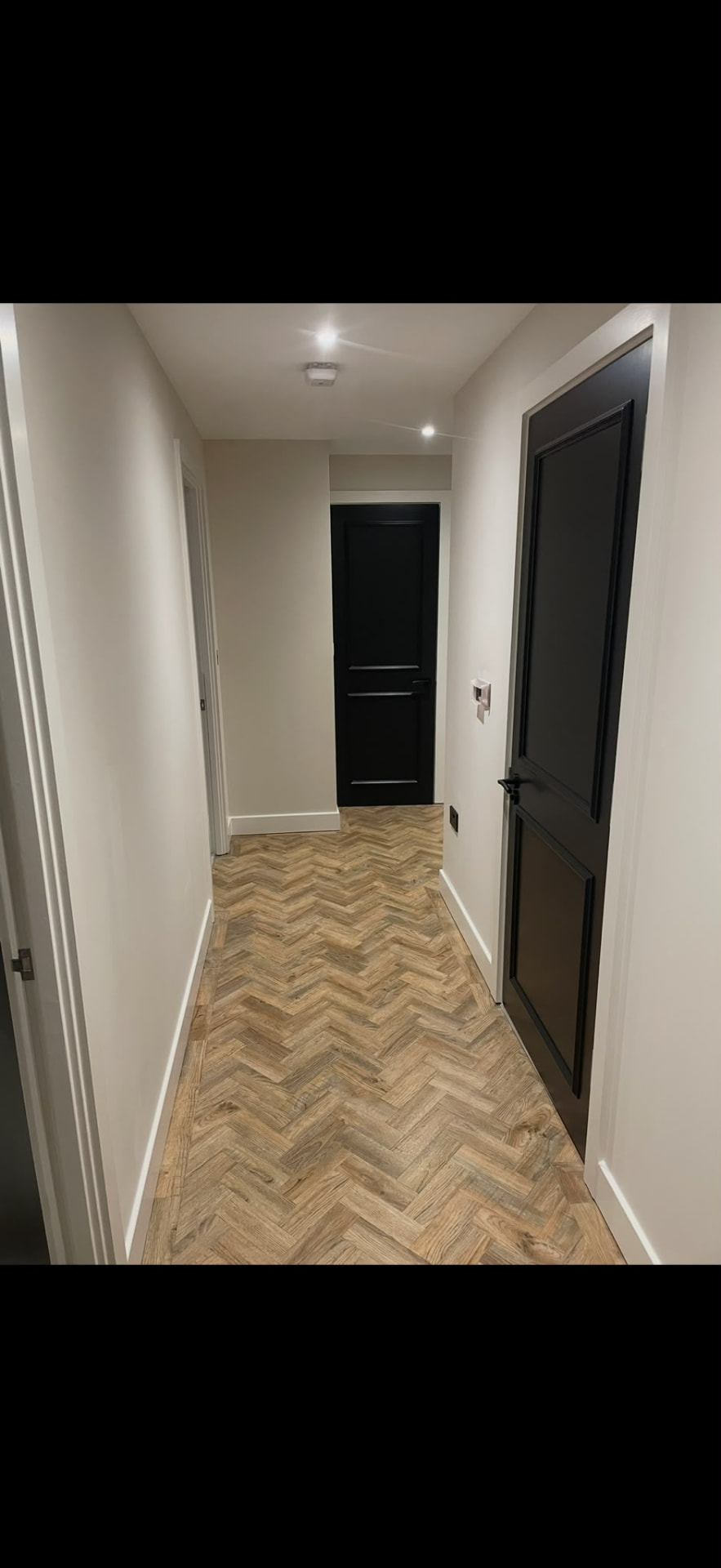 Corridor with black painted door, white walls and herringbone flooring, Brighton